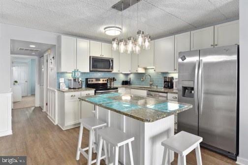 kitchen featuring pendant lighting, stainless steel appliances, a center island, white cabinets, and a kitchen bar