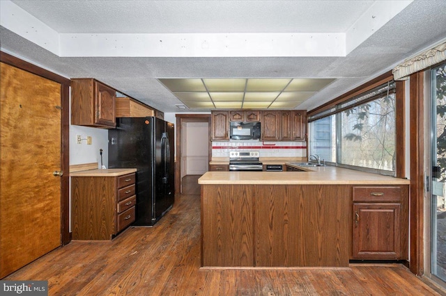 kitchen with a sink, black appliances, dark wood finished floors, and light countertops