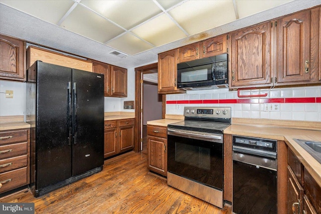 kitchen featuring black appliances, wood finished floors, tasteful backsplash, and light countertops