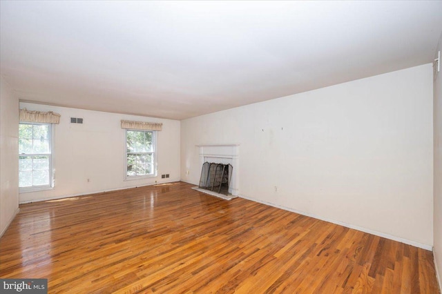 unfurnished living room with visible vents, wood finished floors, a healthy amount of sunlight, and a fireplace with raised hearth