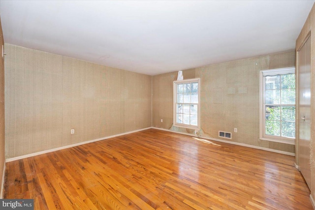 empty room featuring visible vents, baseboards, light wood-style flooring, and wallpapered walls