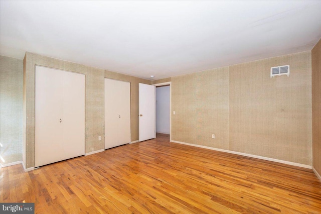 unfurnished bedroom with wood finished floors, visible vents, two closets, and baseboards