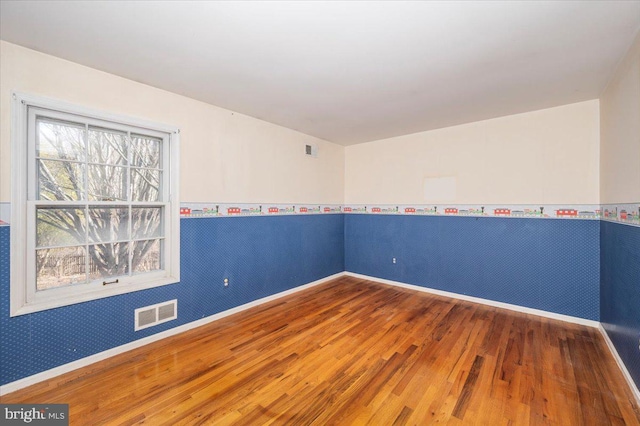 empty room featuring visible vents, wallpapered walls, baseboards, and wood finished floors