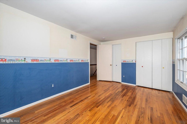 unfurnished bedroom with visible vents, baseboards, wood finished floors, and wallpapered walls