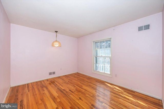 empty room featuring light wood-type flooring, visible vents, and baseboards