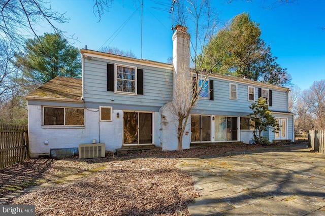 view of front of property with cooling unit, brick siding, a chimney, and fence