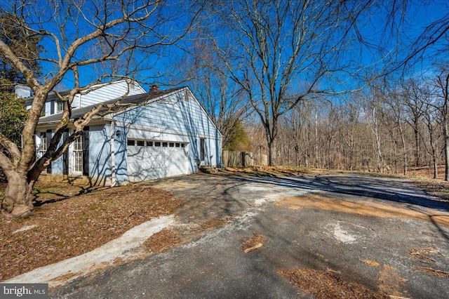 view of side of home featuring driveway, a chimney, and a garage