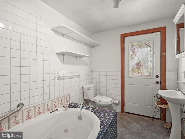3137 18th St NE, Washington, DC 20018 - bathroom with tile walls, toilet, a wainscoted wall, a tub with jets, and tile patterned flooring