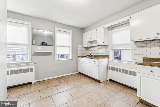 kitchen featuring dark countertops, decorative backsplash, white cabinets, and radiator