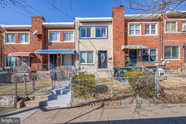 townhome / multi-family property with brick siding, a fenced front yard, a chimney, and a gate