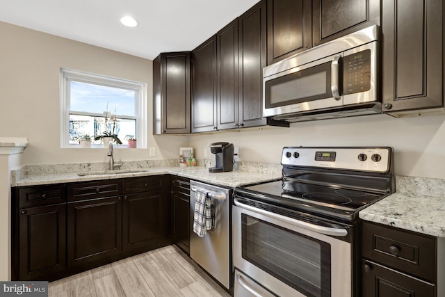 kitchen featuring light stone countertops, stainless steel appliances, light wood-type flooring, a sink, and recessed lighting