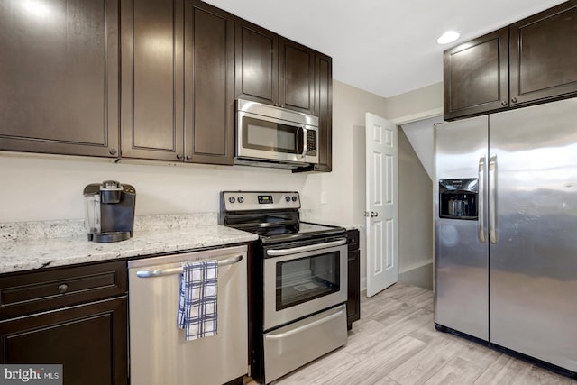 kitchen featuring recessed lighting, light wood-style flooring, appliances with stainless steel finishes, dark brown cabinets, and light stone countertops