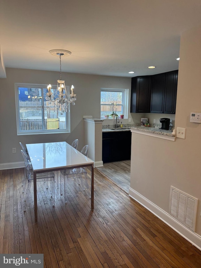 unfurnished dining area featuring a sink, visible vents, baseboards, hardwood / wood-style floors, and an inviting chandelier