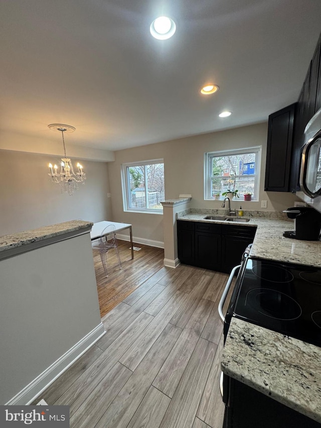 kitchen with light wood finished floors, dark cabinetry, a sink, and light stone counters