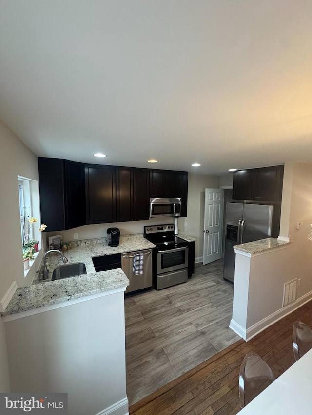 kitchen with light wood finished floors, dark cabinets, stainless steel appliances, and a sink