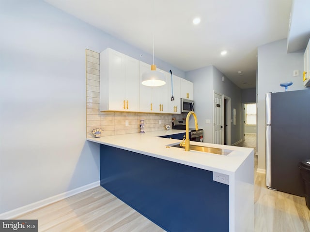 kitchen featuring white cabinets, appliances with stainless steel finishes, a peninsula, light countertops, and pendant lighting