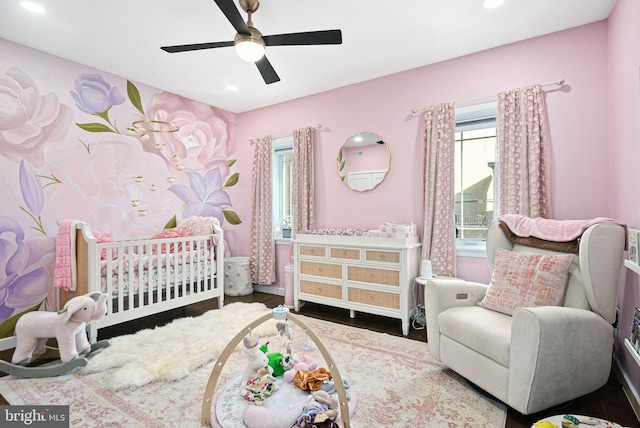 bedroom with hardwood / wood-style flooring, a crib, and ceiling fan