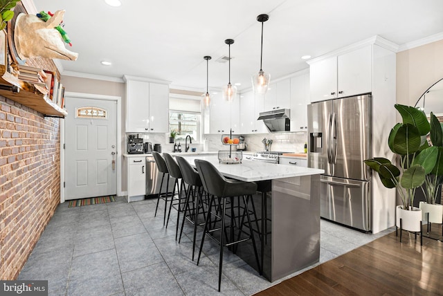 kitchen featuring a center island, ornamental molding, appliances with stainless steel finishes, pendant lighting, and white cabinets