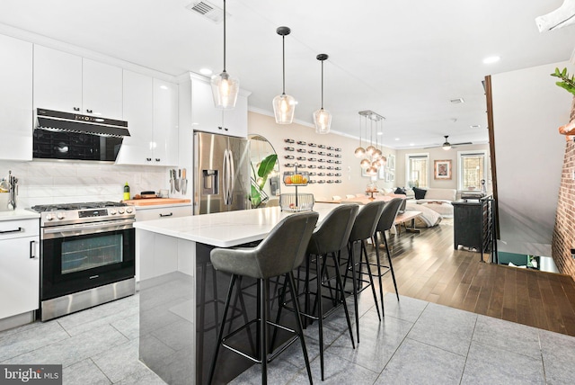 kitchen with pendant lighting, range hood, white cabinets, a kitchen breakfast bar, and stainless steel appliances