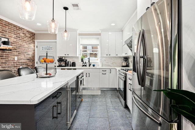 kitchen with brick wall, white cabinetry, hanging light fixtures, stainless steel appliances, and crown molding