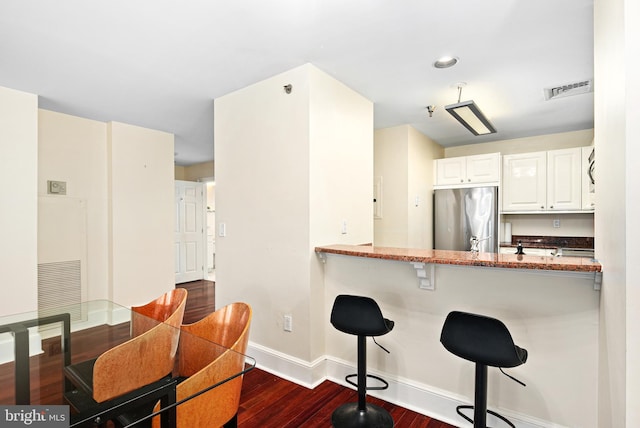 kitchen featuring dark hardwood / wood-style floors, a breakfast bar area, white cabinets, stainless steel fridge, and kitchen peninsula