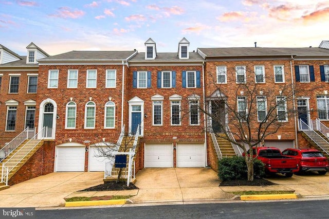 townhome / multi-family property featuring stairway, an attached garage, brick siding, and driveway