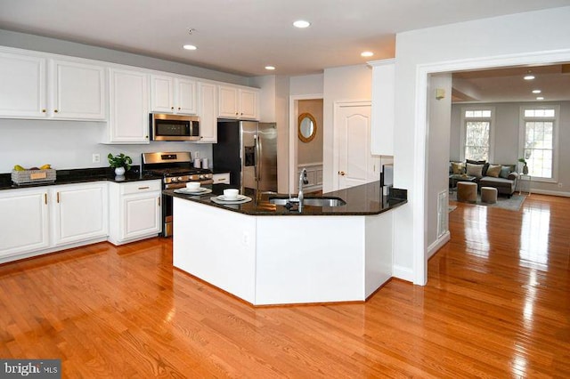 kitchen featuring a peninsula, light wood-style flooring, a sink, stainless steel appliances, and white cabinetry