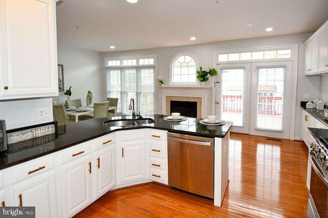 kitchen with a fireplace, a sink, white cabinets, appliances with stainless steel finishes, and light wood-type flooring