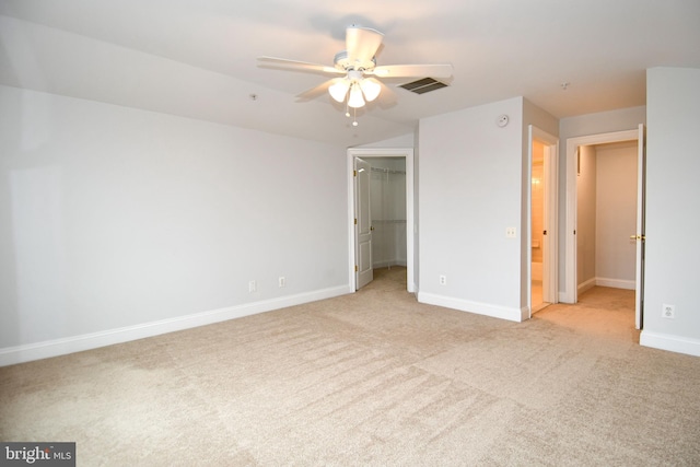 unfurnished bedroom with a ceiling fan, baseboards, a closet, a walk in closet, and light colored carpet