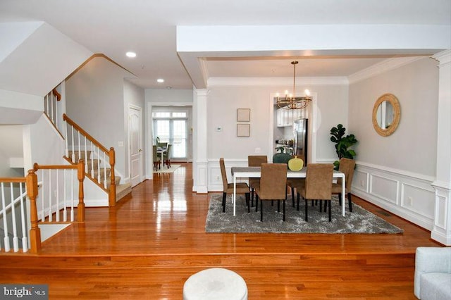 dining area with ornamental molding, wood finished floors, wainscoting, a decorative wall, and stairs