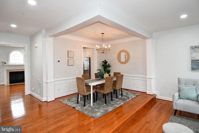 dining room with a notable chandelier, light wood-type flooring, and ornate columns