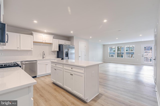 kitchen with a kitchen island, sink, white cabinets, stainless steel appliances, and light hardwood / wood-style flooring