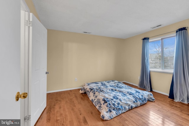 bedroom with light wood-style flooring, visible vents, and baseboards