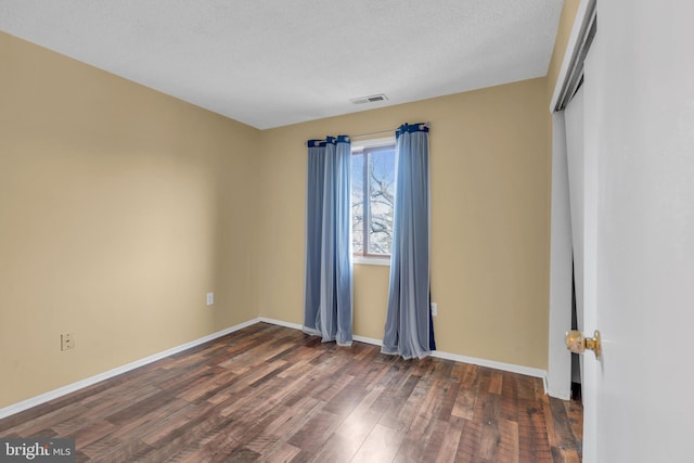 spare room with dark wood-type flooring, visible vents, a textured ceiling, and baseboards