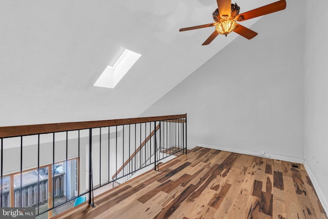 interior space with vaulted ceiling with skylight, baseboards, wood finished floors, and an upstairs landing