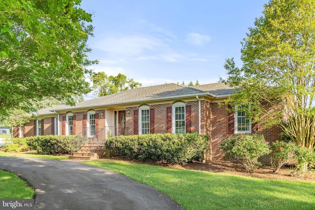 ranch-style house featuring a shingled roof, a front yard, and brick siding