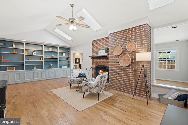 sitting room with light wood-type flooring, a brick fireplace, ceiling fan, and vaulted ceiling with skylight