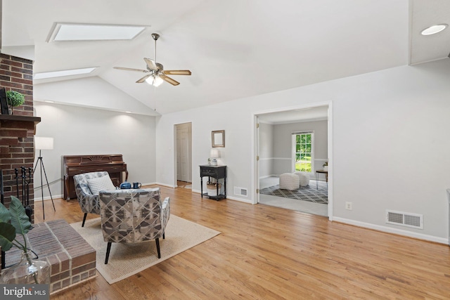 living area with a brick fireplace, vaulted ceiling with skylight, visible vents, and wood finished floors