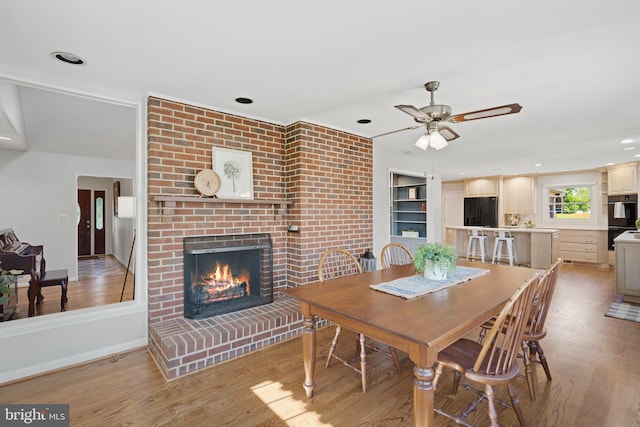 dining room with a brick fireplace, light wood-style flooring, baseboards, and recessed lighting