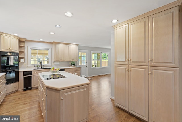 kitchen featuring light wood-type flooring, black appliances, a sink, and light brown cabinetry