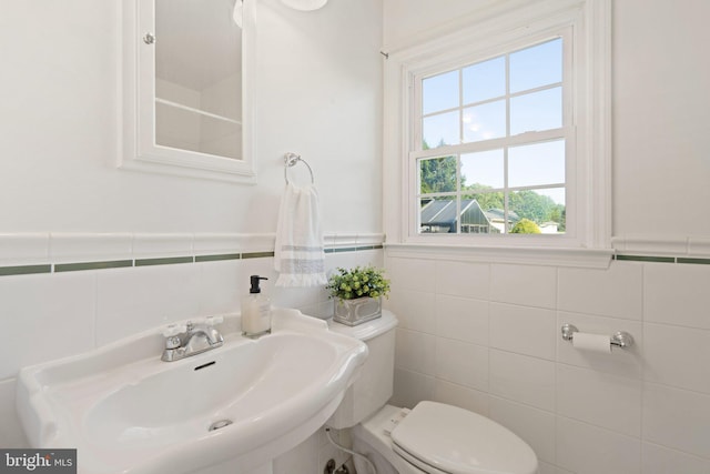 bathroom featuring toilet, tile walls, a sink, and wainscoting