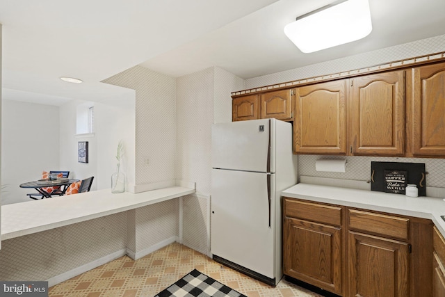 kitchen featuring light countertops, freestanding refrigerator, decorative backsplash, light floors, and brown cabinetry