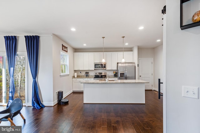 kitchen with white cabinets, appliances with stainless steel finishes, a kitchen island with sink, and pendant lighting