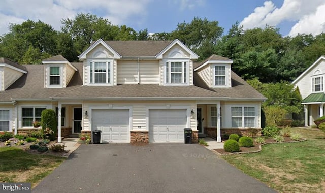 townhome / multi-family property with aphalt driveway, a front yard, roof with shingles, stone siding, and an attached garage