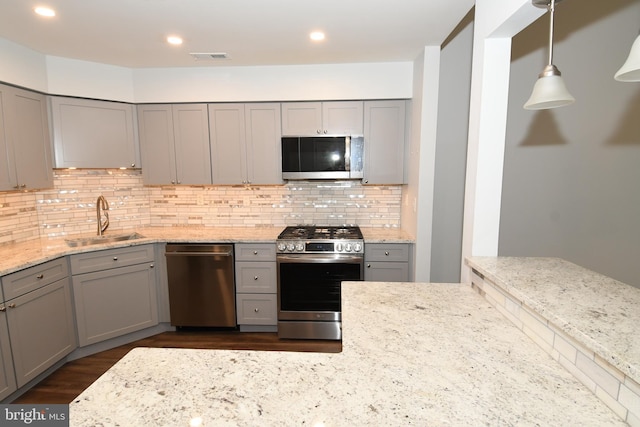 kitchen with gray cabinets, a sink, backsplash, appliances with stainless steel finishes, and light stone countertops