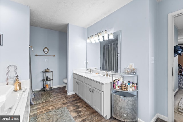 full bath with a sink, a textured ceiling, double vanity, and wood finished floors