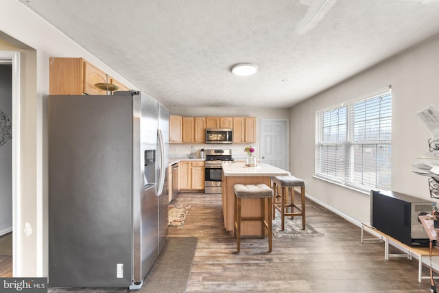 kitchen featuring dark wood-style floors, a center island, a breakfast bar area, stainless steel appliances, and light countertops