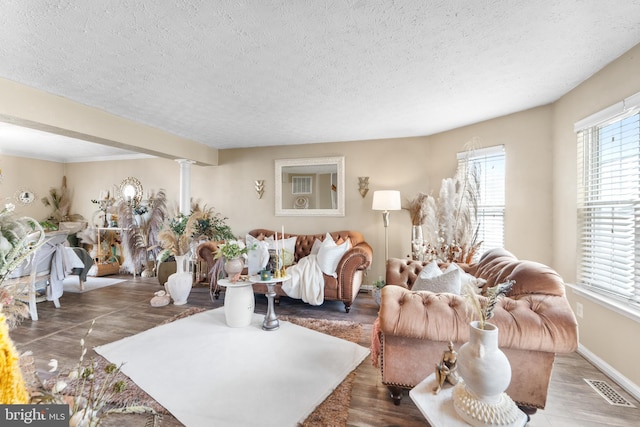 living room featuring baseboards, visible vents, a textured ceiling, and ornate columns