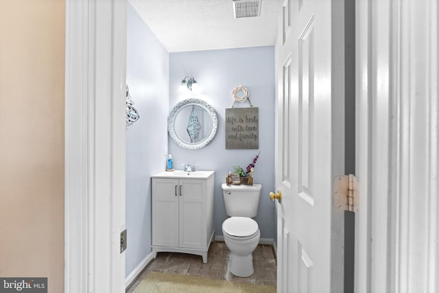 bathroom with a textured ceiling, toilet, vanity, visible vents, and baseboards