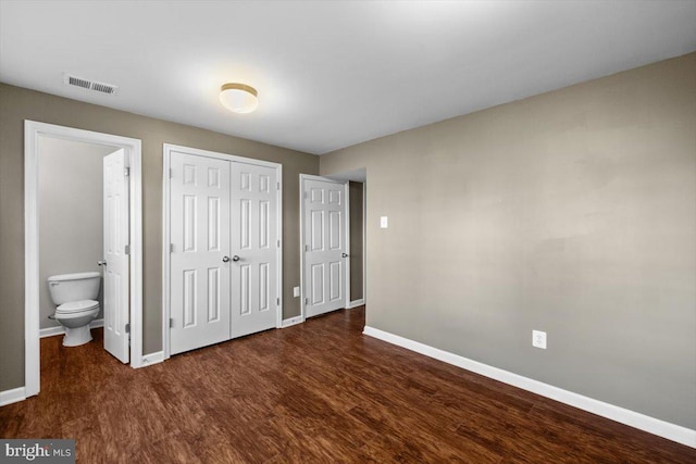 unfurnished bedroom featuring ensuite bathroom, dark hardwood / wood-style floors, and a closet